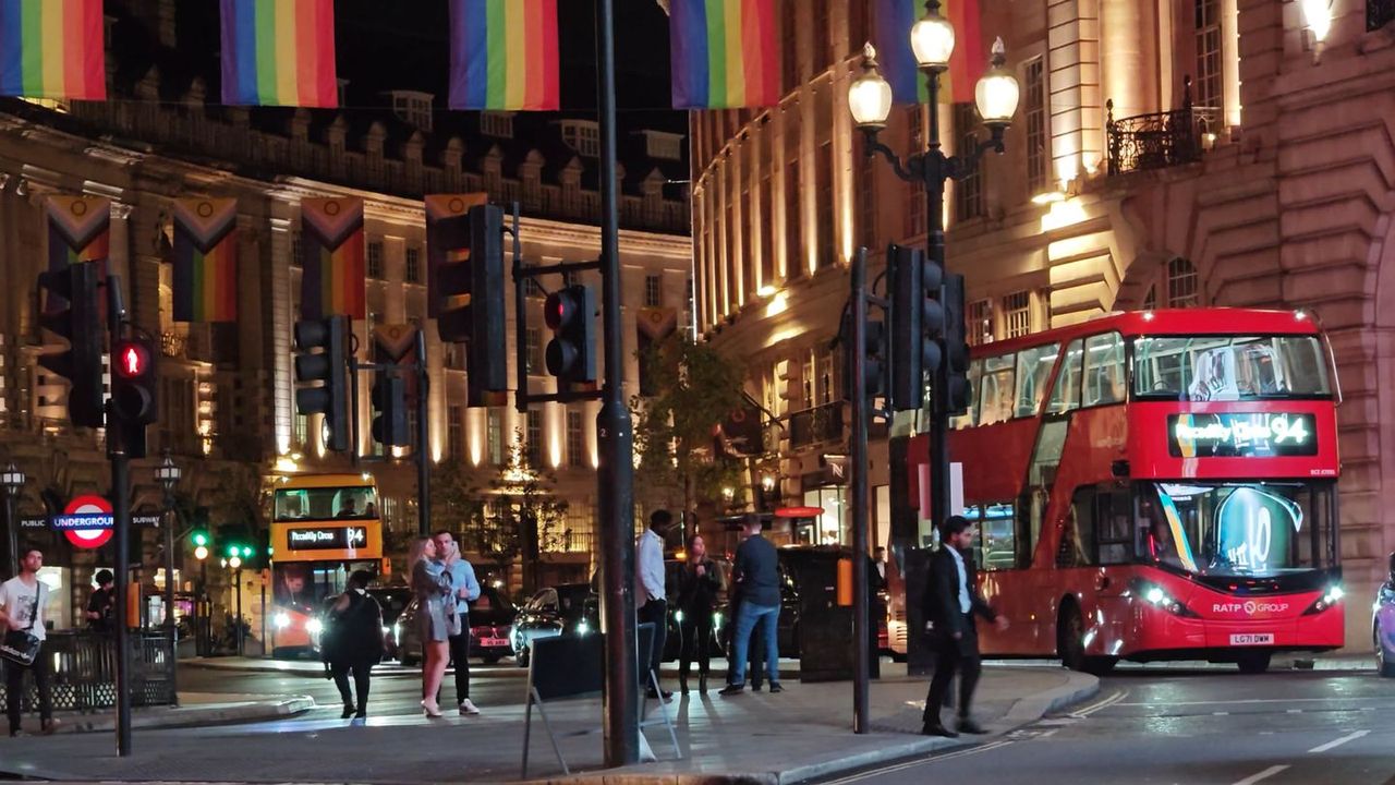 A red double-decker bus on Regent Street at dusk, with flags strung above the road and lit shop windows