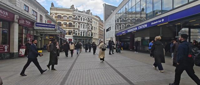 People walking along a pedestrian street past the Elizabeth line entrance at Farringdon station