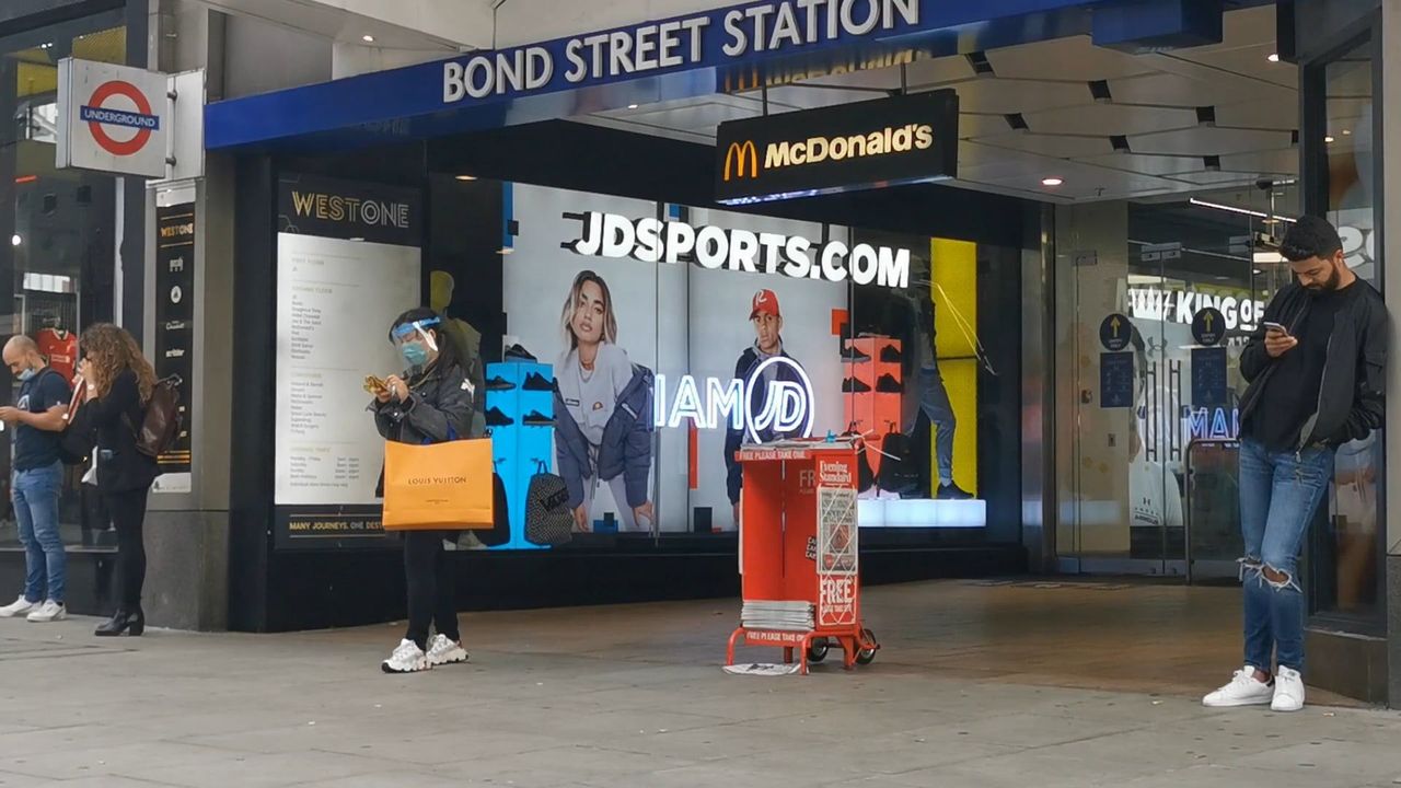 The Bond Street Station frontage on a shopping street in daytime, with an Underground roundel and people waiting outside