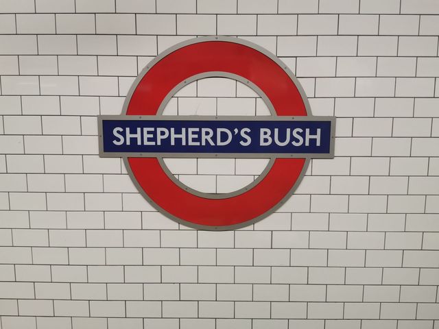 A red Underground roundel reading Shepherd's Bush on a white tiled wall